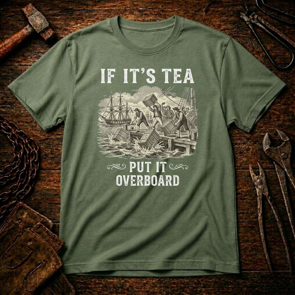 An olive green crewneck t-shirt with a vintage-style nautical graphic and the text 'IF IT'S TEA PUT IT OVERBOARD', displayed flat on a rustic wooden background with tools.