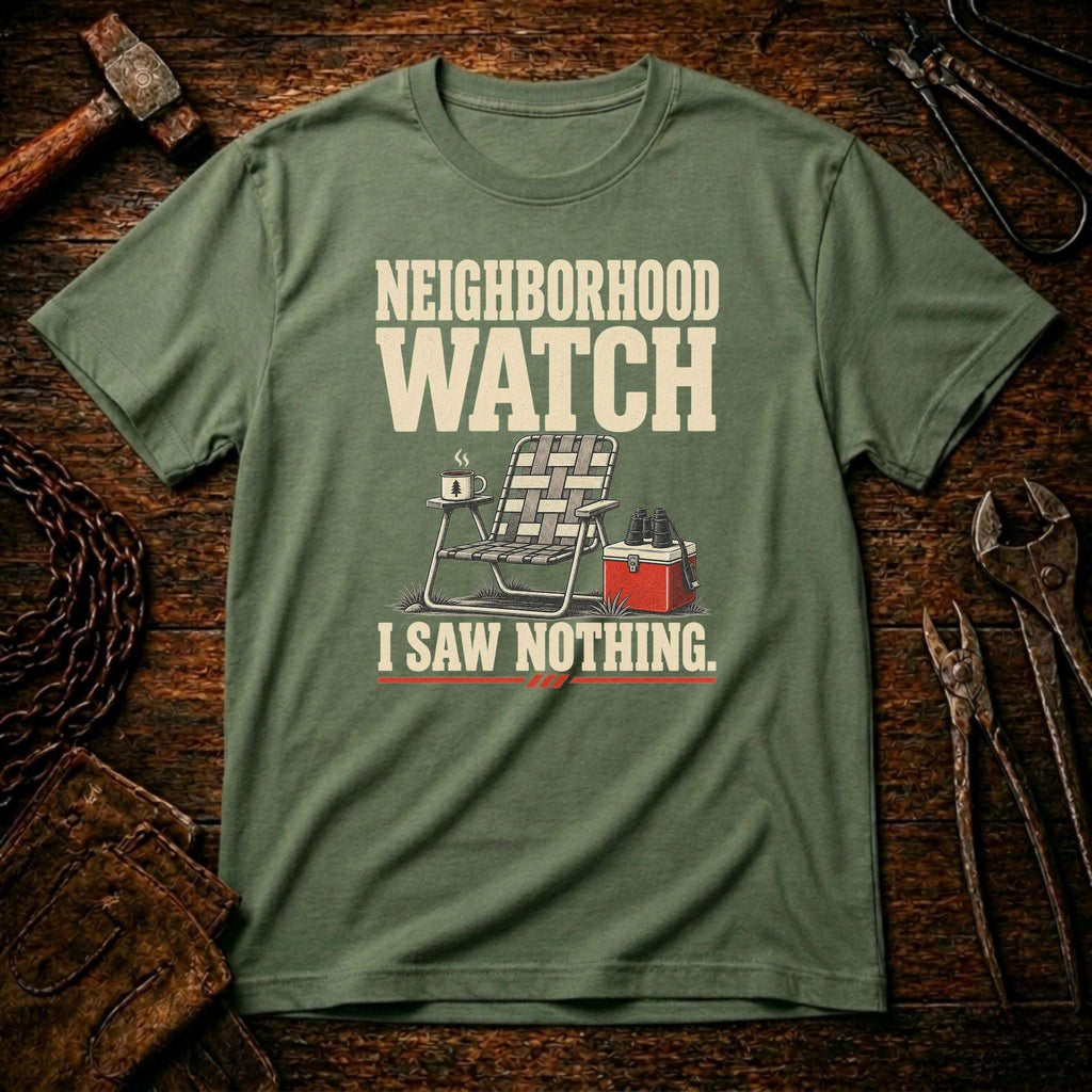A military green graphic t-shirt laid flat on a rustic wooden background with tools like a hammer, chain, and wrenches. The shirt features a cream-colored graphic that reads 'NEIGHBORHOOD WATCH I SAW NOTHING.