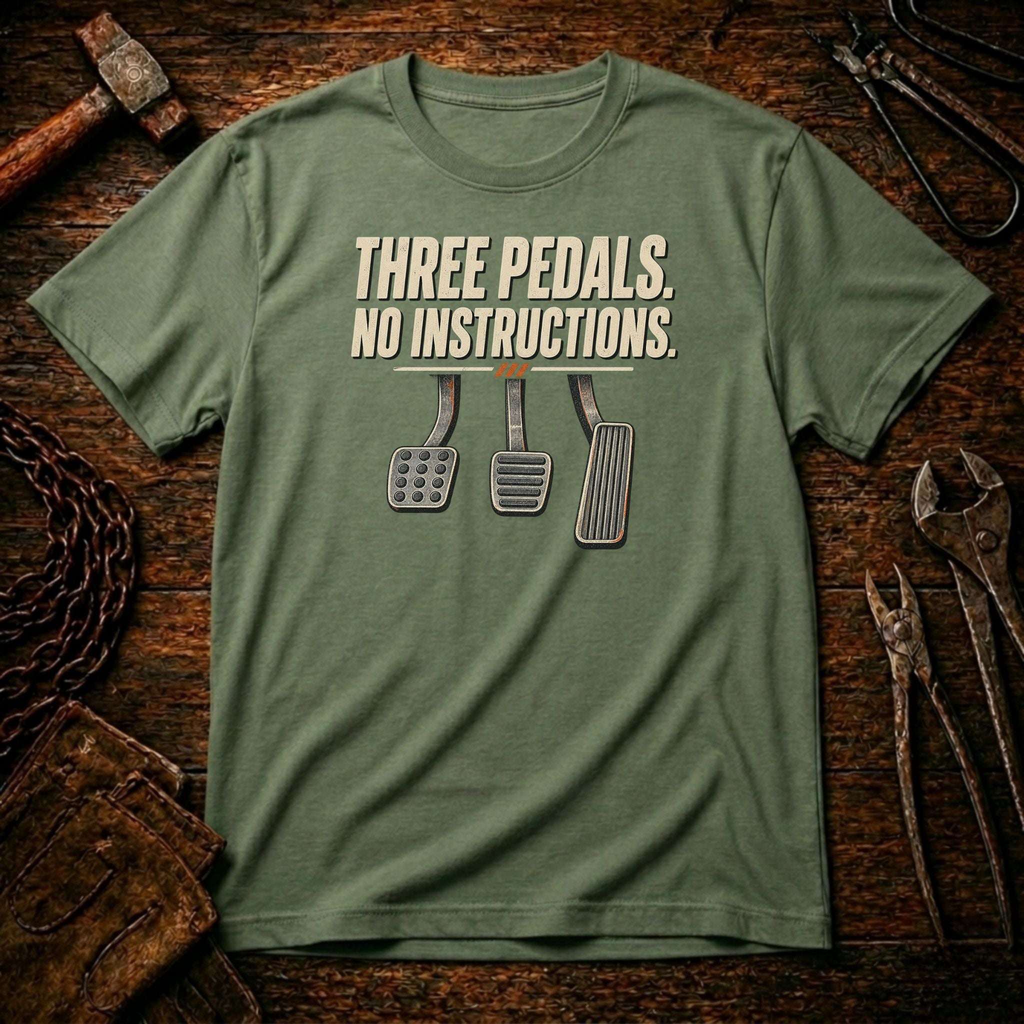 A military green crewneck t-shirt with a graphic print reading 'THREE PEDALS. NO INSTRUCTIONS.