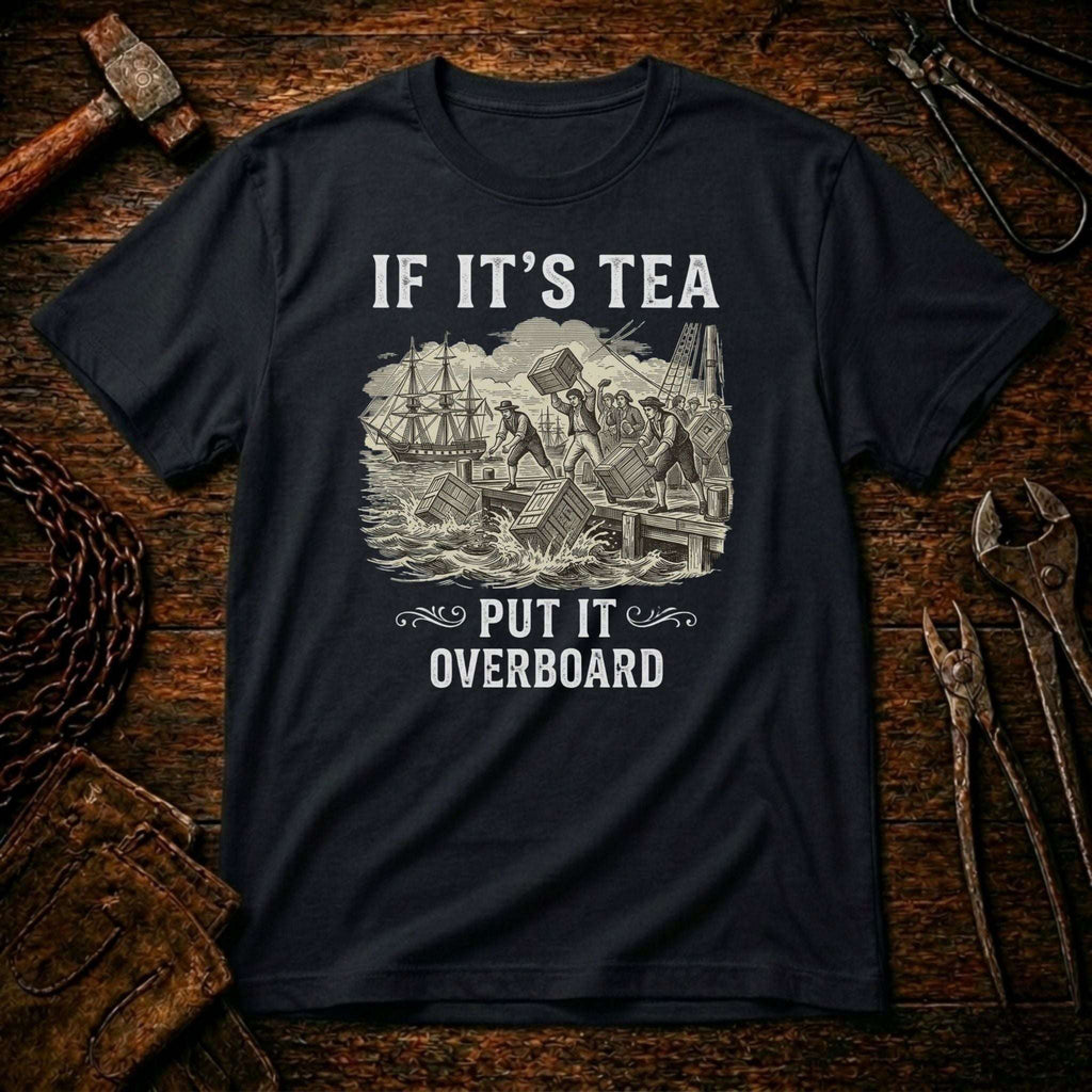 A black crewneck t-shirt with a vintage-style nautical graphic and the text 'IF IT'S TEA PUT IT OVERBOARD', displayed flat on a rustic wooden background with tools.