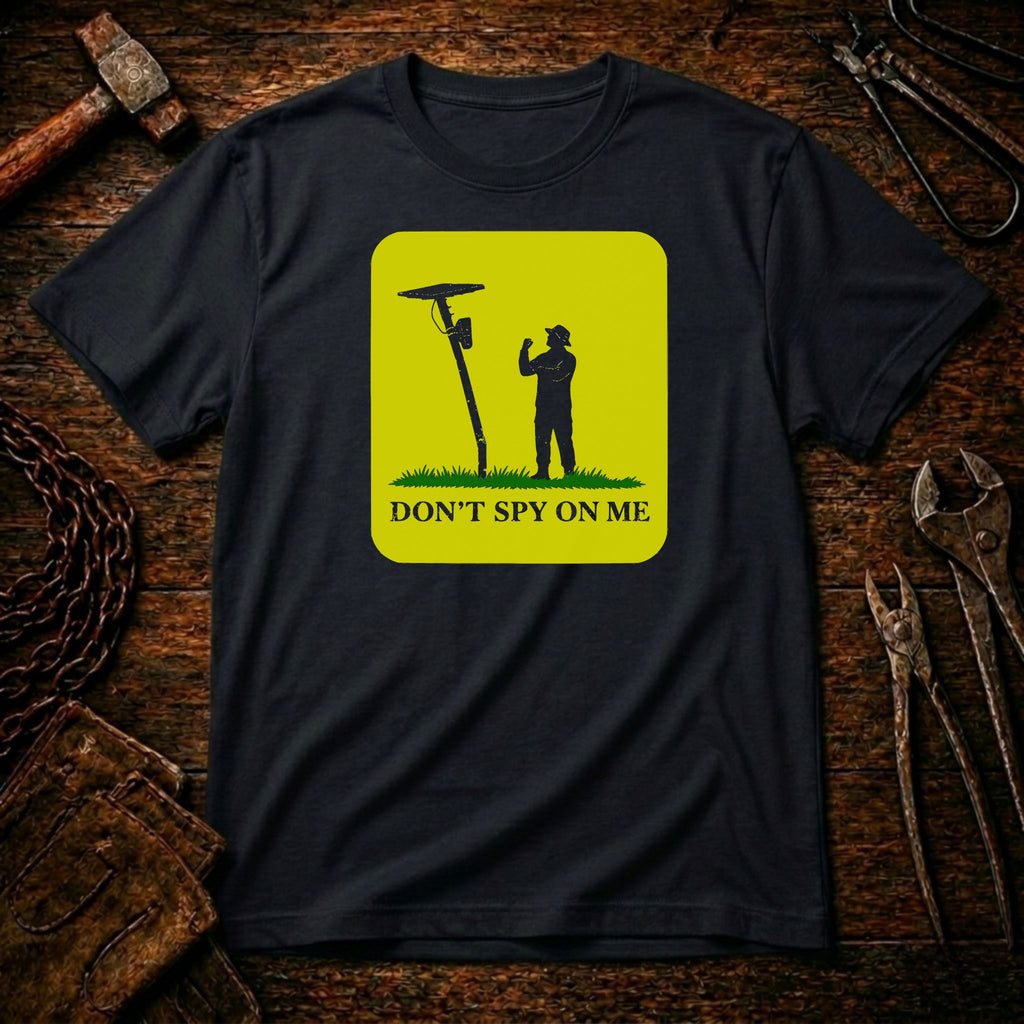 A black short-sleeve t-shirt with a bright yellow square graphic on the chest. The graphic shows a black silhouette of a person standing next to a spy radio antenna with the text 'DON'T SPY ON ME' below.