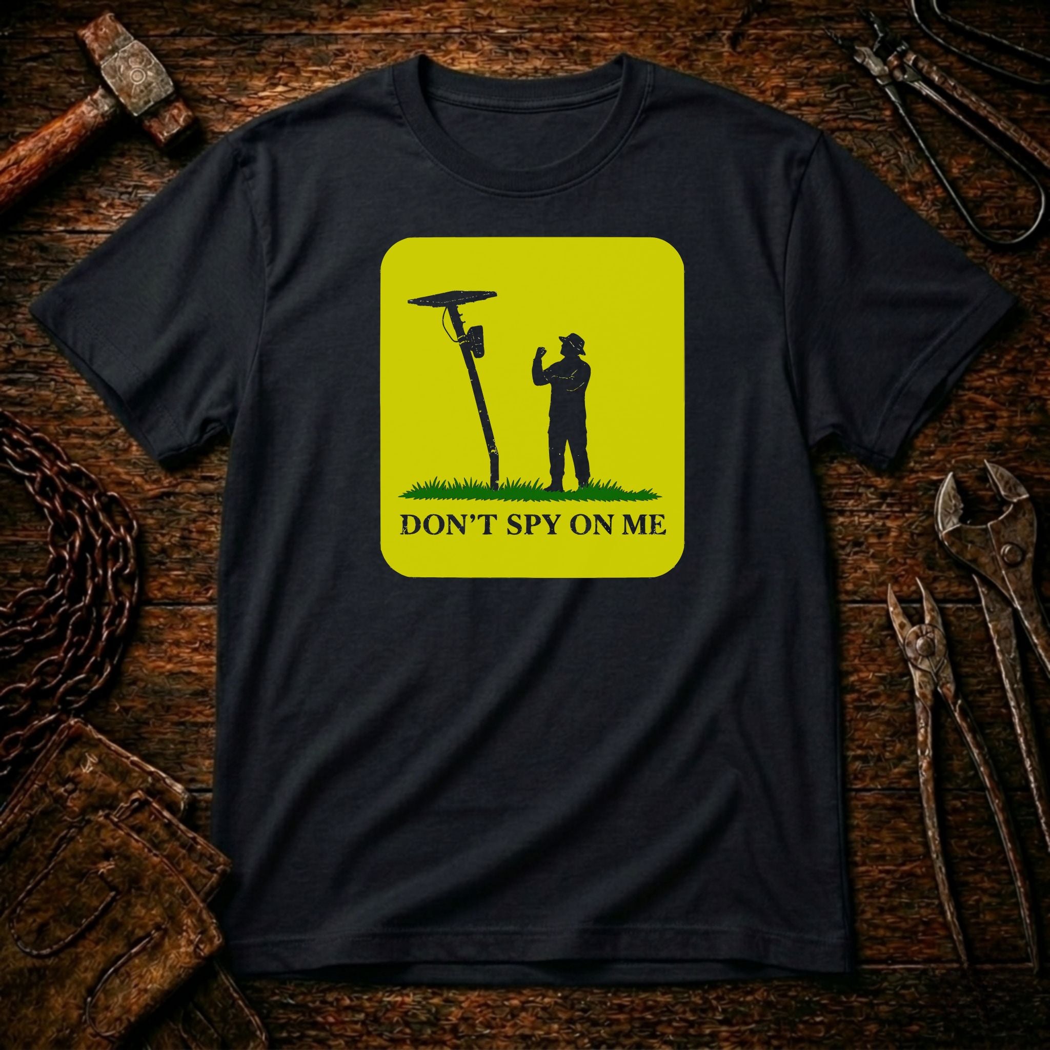 A black short-sleeve t-shirt with a bright yellow square graphic on the chest. The graphic shows a black silhouette of a person standing next to a spy radio antenna with the text 'DON'T SPY ON ME' below.