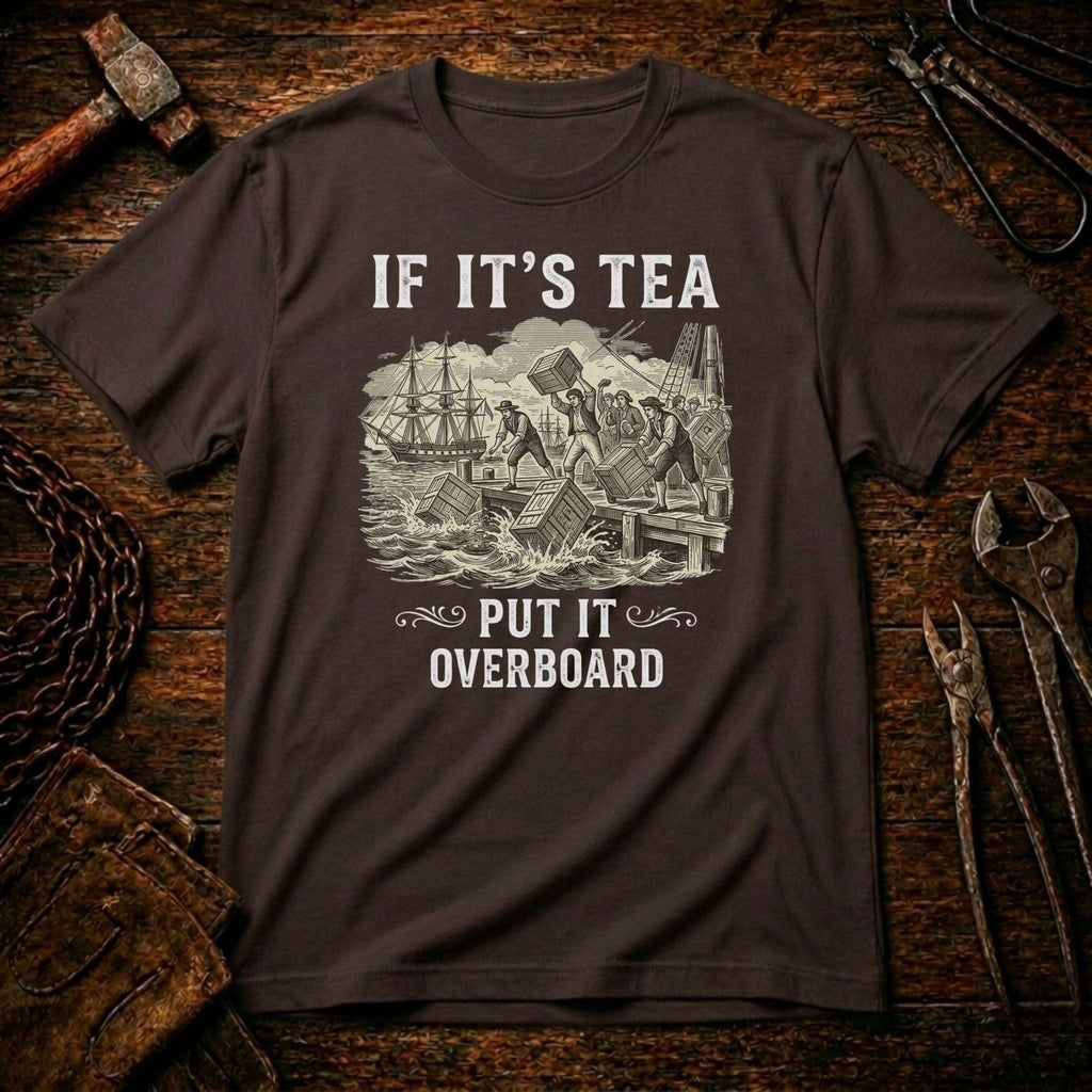 A dark brown short-sleeve t-shirt with a vintage-style white graphic print of a shipwreck and the text 'IF IT'S TEA PUT IT OVERBOARD'. The shirt is displayed flat on a rustic wooden background surrounded by tools like a hammer, wrenches, and pliers.