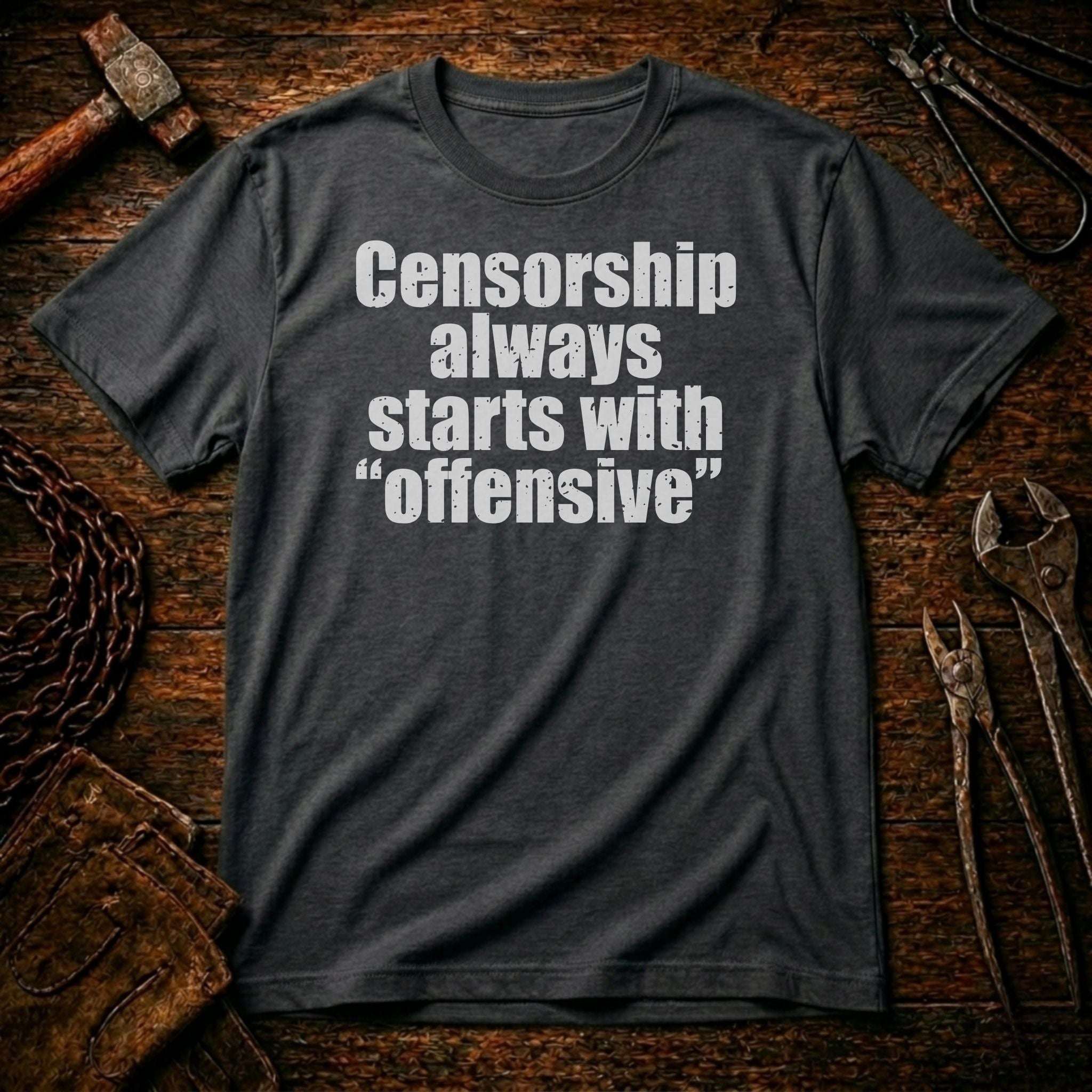 Gray t-shirt with text 'Censorship always starts with offensive' on a rustic wooden background.