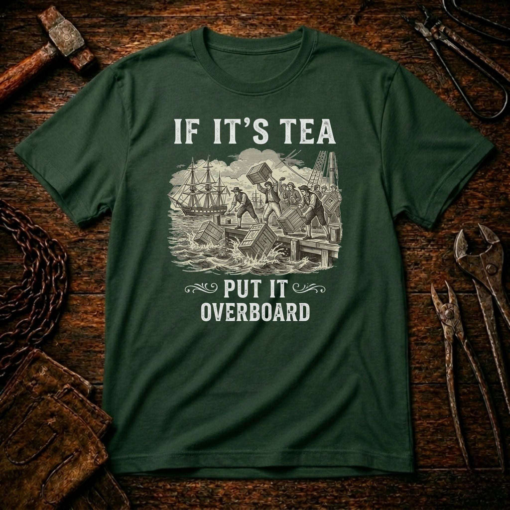 A dark green crewneck t-shirt with a vintage-style white graphic of ships and the text 'IF IT'S TEA PUT IT OVERBOARD', displayed flat on a rustic wooden background with tools.