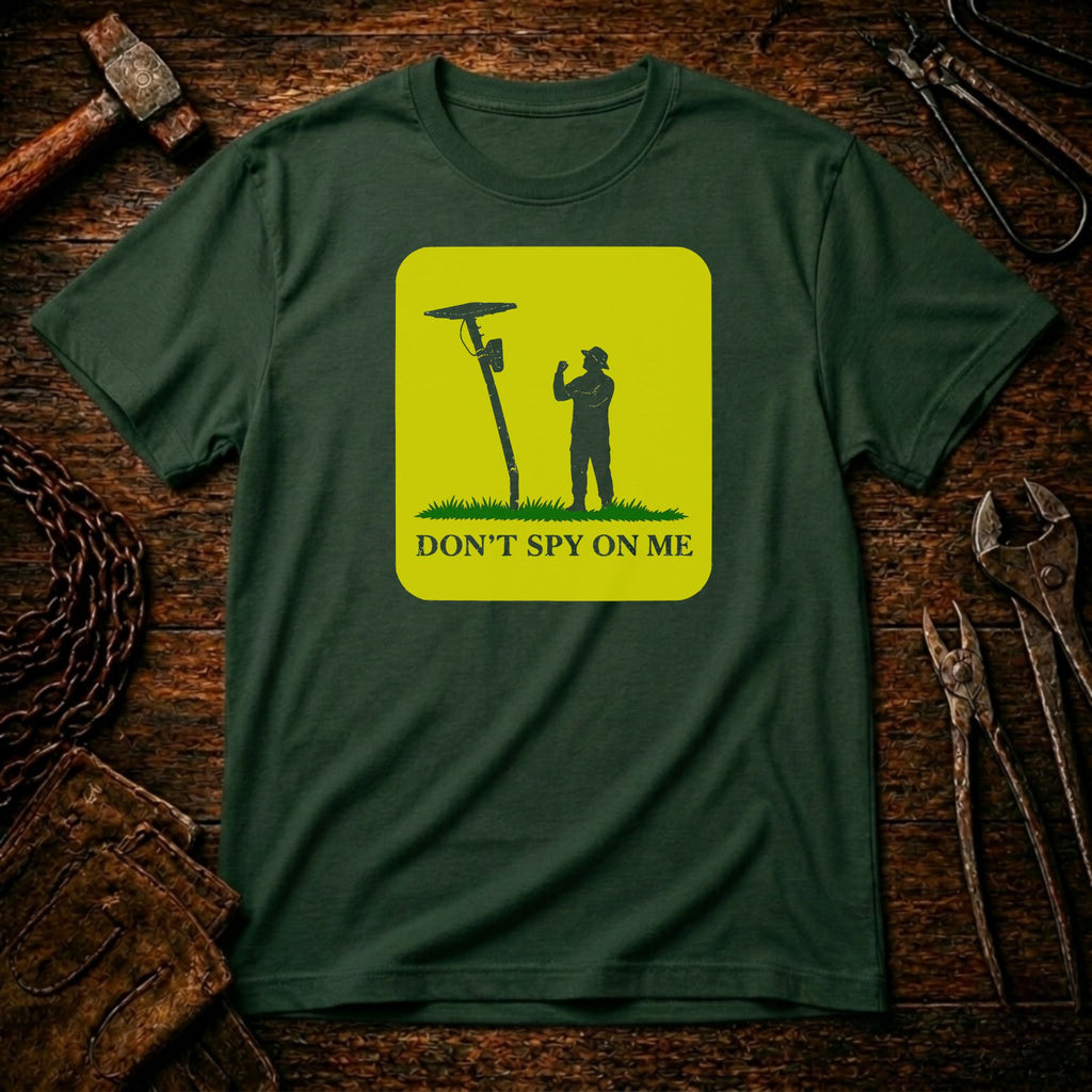 A dark green crewneck t-shirt with a bright yellow-green square graphic on the chest. The graphic shows a silhouette of a person holding a spy camera next to a lamp post, with the text 'DON'T SPY ON ME' below.